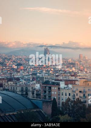 Una serena vista dell'alba su Barcellona, che mette in risalto la Sagrada Familia in un esteso paesaggio urbano con montagne lontane. Foto Stock