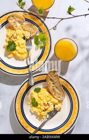 Due piatti vivaci con soffici uova strapazzate con erbe aromatiche e pane tostato accanto al succo d'arancia rinfrescante. Una deliziosa e invitante scena colazioni con Foto Stock