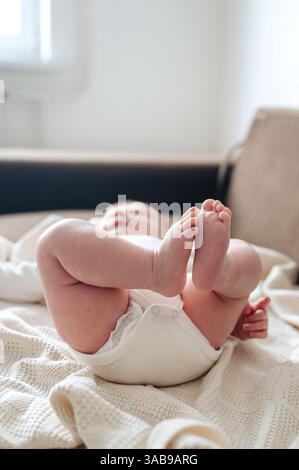 Un'immagine serena di una bambina appena nata sdraiata su una morbida coperta a maglia. I suoi piccoli piedi sono giocosamente sollevati, catturando l'innocenza e il calore dell'infa Foto Stock