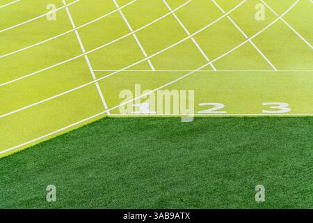 Una vista luminosa e dettagliata delle linee di partenza numerate da uno a tre su una pista di atletica verde in uno stadio all'aperto, a simboleggiare la prontezza e la competizione. Foto Stock