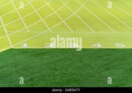 Un dettagliato primo piano delle linee di partenza numerate dai colori vivaci, da 1 a 5, su una pista sintetica verde in uno stadio di atletica all'aperto, che mostra il c Foto Stock
