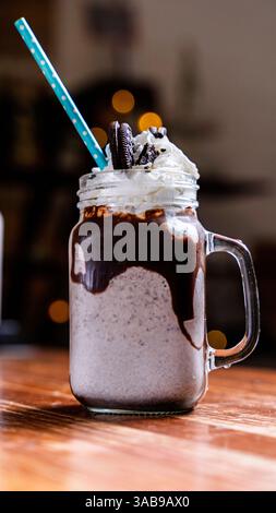 Un delizioso frullato al cioccolato in un barattolo mason con panna montata e biscotti. La consistenza cremosa e i sapori ricchi lo rendono un caffè perfetto Foto Stock