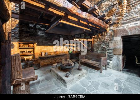Cucina rustica tradizionale all'interno di una casa di campagna a Lugo, Spagna, con pareti in pietra, travi in legno e utensili antichi. Foto Stock