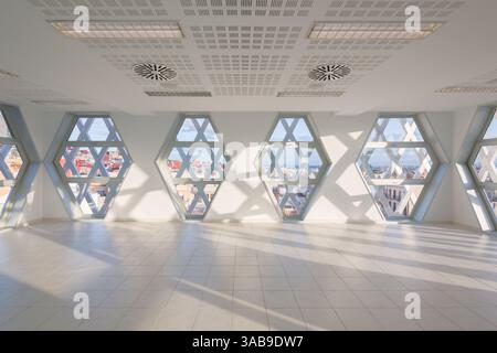 Moderna sala auditorium con finestre esagonali, pareti bianche e pavimento piastrellato. La luce naturale filtra, proiettando ombre geometriche, con una città Foto Stock