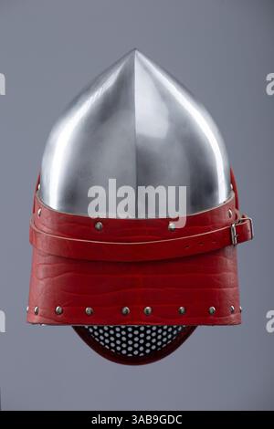 Moderno casco da scherma con visiera protettiva in rete. Un casco in argento lucido è dotato di visiera integrale in mesh ed è fissato con un cinturino in pelle rosso e me Foto Stock