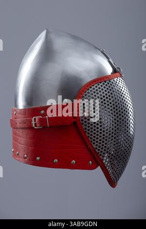 Moderno casco da scherma con visiera protettiva in rete. Un casco in argento lucido è dotato di visiera integrale in mesh ed è fissato con un cinturino in pelle rosso e me Foto Stock