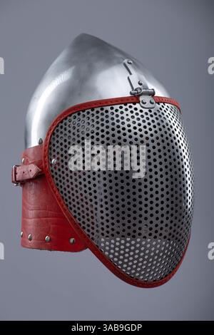 Moderno casco da scherma con visiera protettiva in rete. Un casco in argento lucido è dotato di visiera integrale in mesh ed è fissato con un cinturino in pelle rosso e me Foto Stock