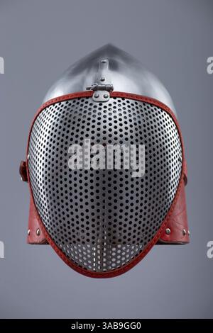 Moderno casco da scherma con visiera protettiva in rete. Un casco in argento lucido è dotato di visiera integrale in mesh ed è fissato con un cinturino in pelle rosso e me Foto Stock