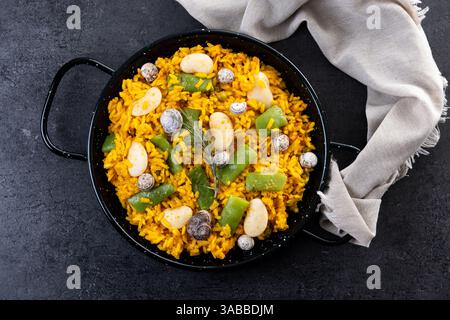 Paella tradizionale valenciana con coniglio, pollo, fagioli di garrofone, lumache, fagioli verdi marocchini e zafferano su sfondo nero. Foto Stock