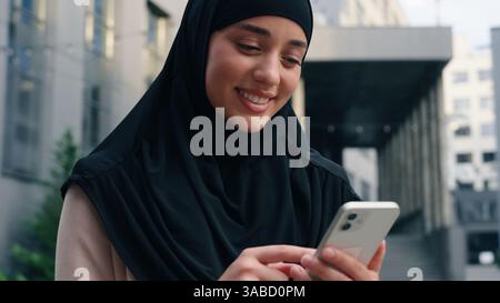 Ritratto felice sorridente musulmana positivo donna islamica che indossa hijab donna d'affari donna d'affari in città all'aperto in centro utilizzando il telefono cellulare Foto Stock