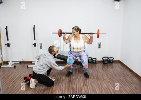 Personal trainer che aiuta il cliente ad allenarsi con lo squat dei pesi in palestra Foto Stock