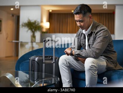 Il viaggiatore attende nella hall dell'hotel con i bagagli mentre effettua il check-in Foto Stock