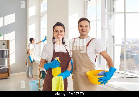 Ritratto di due addetti al servizio pulizie felici che stanno accanto a una finestra pulita e sorridono Foto Stock