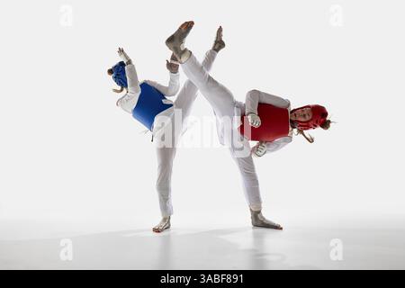 Due atlete di taekwondo in movimento, che combattono con calci sincronizzati sullo sfondo bianco dello studio. Foto Stock