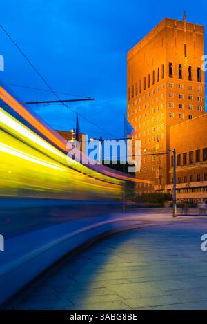 Oslo, Norvegia notturna, vista notturna di un tram cittadino che accelera verso l'edificio del Municipio (Radhus) nel quartiere portuale centrale di Oslo, Norvegia. Foto Stock