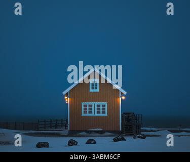 Gelbes Rorbuer-Haus in Sakrisoy auf den Lofoten in Norwegen, eingehüllt in einen tobenden Schneesturm zur blauen Stunde, der den Olstinden verdeckt Foto Stock