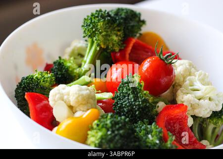 Vivace insalata di verdure fresche con broccoli, pomodori ciliegini, peperoni e cavolfiore in una ciotola bianca. Concetto di alimentazione sana Foto Stock