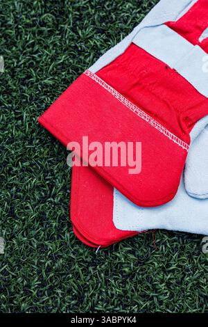 Questa immagine mostra straordinari guanti sportivi rossi e grigi su una vibrante erba artificiale verde, perfetti per mettere in risalto le attrezzature atletiche e gli sport all'aperto Foto Stock