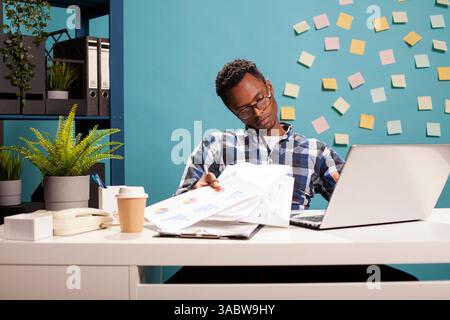 Impiegato stanco negli straordinari, seduto alla scrivania e frustrato di documenti, sopraffatto dal carico di lavoro. Ritratto di un analista finanziario stanco che tiene documenti e guarda in basso nella tristezza. Foto Stock