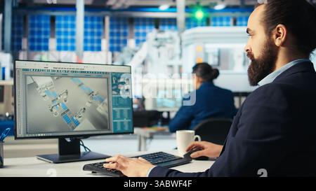 Ingegnere di fabbrica fotovoltaico che regola i parametri del sistema su PC per massimizzare la generazione di energia elettrica a celle solari. Tecnico che ottimizza la fornitura di energia nell'impianto di produzione di pannelli solari, telecamera A. Foto Stock