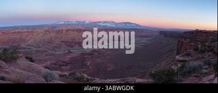 Crepuscolo su un profondo canyon rosso a sud di Moab Utah. Le montagne innevate di la Sal si innalzano in alto in questa sera invernale. Foto Stock