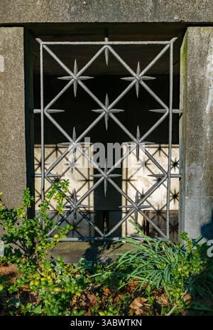 Primo piano verticale di una finestra del mausoleo con barre decorative in ferro al cimitero Dorotheenstadt di Berlino, germe., con ombre proiettate dalla luce del sole pomeridiano. Foto Stock