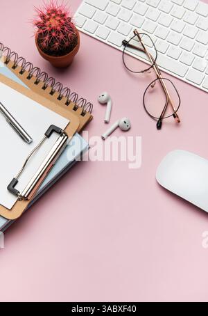 Forniture per ufficio e dispositivi tecnologici disposti in modo ordinato su un desktop rosa, creando uno spazio di lavoro ideale per la produttività e la concentrazione Foto Stock