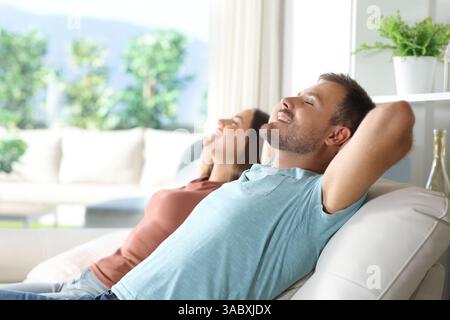 Coppia felice seduta e rilassante seduta su un divano a casa accanto a una finestra con vista sulla terrazza Foto Stock