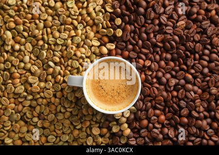 Vista dall'alto di una tazza di caffè espresso cremoso sullo sfondo di chicchi di caffè crudi e tostati in un ambiente artistico. Foto Stock