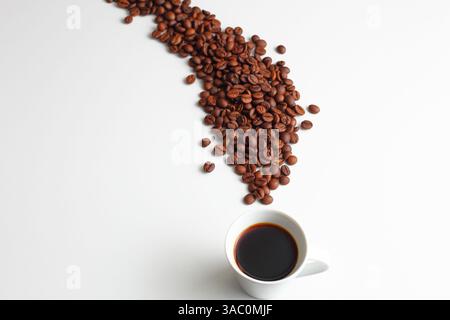 Una tazza di caffè appena estratto accanto ai chicchi tostati sparsi su uno sfondo bianco pulito, che mostra freschezza, energia e design minimalista Foto Stock