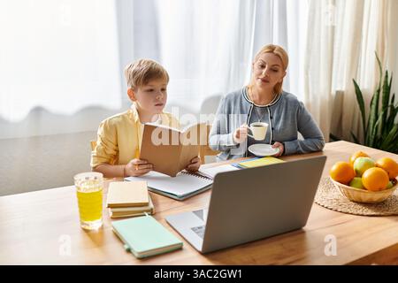 La madre ama il tè mentre suo figlio legge un libro, favorendo un momento di apprendimento insieme. Foto Stock