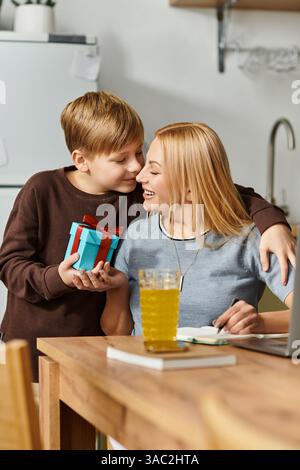 Una madre gioiosa e suo figlio condividono un momento amorevole al tavolo della cucina con un dono. Foto Stock