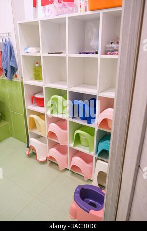 Un bagno con uno scaffale bianco pieno di colorate poltrone in plastica. Lo scaffale è pieno di sedili WC di diversi colori, tra cui rosa, blu e gr Foto Stock