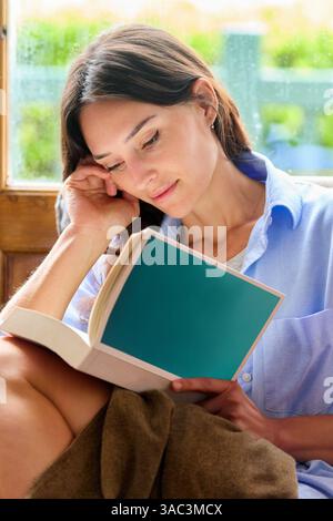 donna di 35 anni a casa, che legge un libro Foto Stock