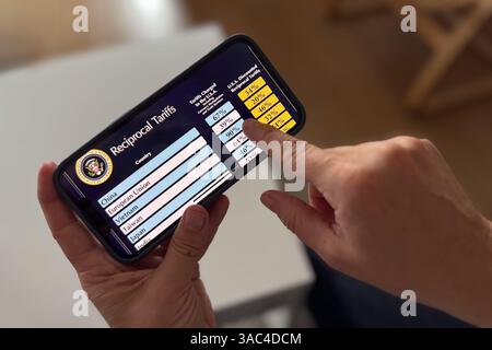 Mani di una persona che controlla l’elenco delle tariffe reciproche di Trump per il giorno della liberazione sullo schermo dello smartphone Foto Stock