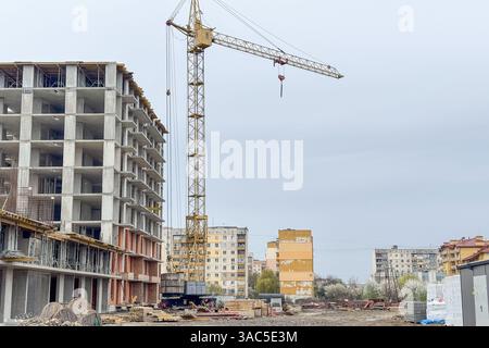 Accanto a una struttura in cemento parzialmente costruita in un cantiere si trova una gru da costruzione Foto Stock
