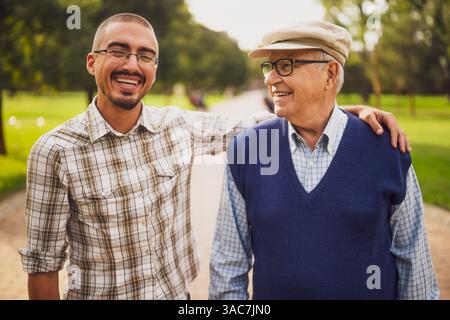 Ritratto di allegro nonno e nipote nel parco. Stanno godendo la giornata di sole e abbracciano. Foto Stock