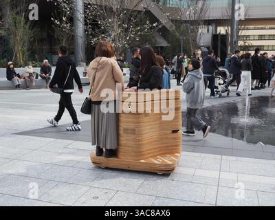 TOKYO, GIAPPONE - 30 marzo 2025: Vista del Gateway Park a Takanawa Gateway City con persone a bordo di un veicolo autonomo iino davanti a una fontana. Foto Stock