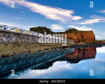 Una fila colorata di rifugi sulla spiaggia e promontorio di Red Sandstone Hollicombe Head, Preston Sands, Paignton, Torbay, Devon. Foto Stock