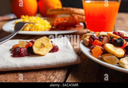 Mix di frutta secca, succo d'arancia rinfrescante e soffici uova strapazzate che creano una colazione vivace e nutriente su un rustico tavolo in legno, perfetta per le mattine energizzanti Foto Stock