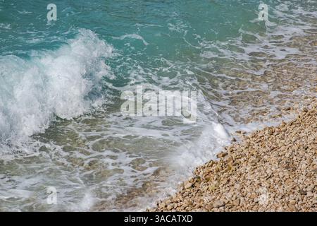 Bellissima spiaggia di ciottoli con onde e cielo blu. Rilassante panorama aereo, vacanze estive. Banner modello festività. Onde surf con un meraviglioso oceano blu l Foto Stock
