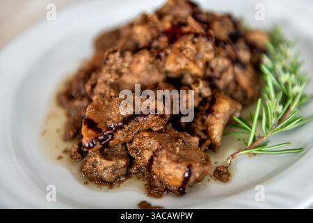 Bocconcini di carne di maiale di cinghiale in salsa di aceto balsamico, erbe di rosmarino su piatto bianco piatto tradizionale sardo in Sardegna Foto Stock