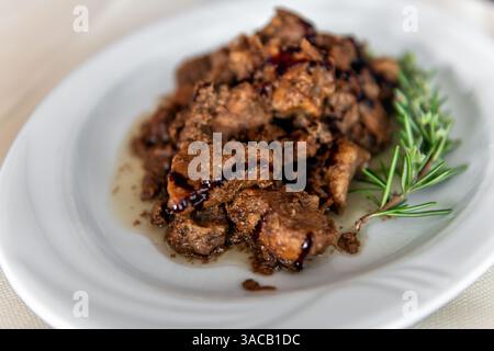 Bocconcini di carne di maiale di cinghiale in salsa di aceto balsamico, erbe di rosmarino su piatto bianco come piatto tradizionale in Sardegna Foto Stock