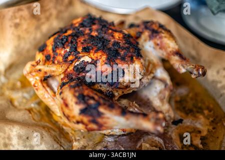 Pollo intero arrosto su forno di carta pergamena, proteine cotte al forno bruciate cibo nero con erbe spezie croccanti pelle dorata Foto Stock