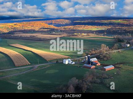 Colline ondulate e campi lussureggianti nella parte settentrionale dello stato di New York, che mostrano i ricchi colori del fogliame autunnale. Una fattoria con silos e fienili si trova pacificamente in mezzo a. Foto Stock