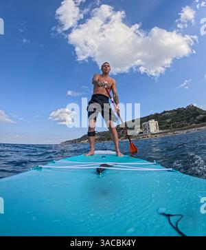 Uomo italiano che fa stand up paddle surf nel Mediterraneo al largo della costa siciliana Foto Stock