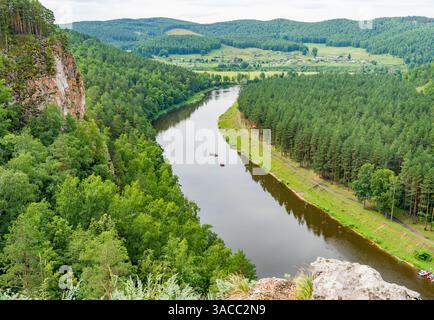 Vista aerea mozzafiato che cattura i turisti in canoa su un tranquillo fiume, incorniciato da lussureggianti foreste verdi e maestose scogliere Foto Stock
