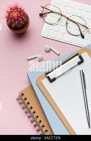 Forniture per ufficio e dispositivi tecnologici disposti in modo ordinato su un desktop rosa, creando uno spazio di lavoro ideale per la produttività e la concentrazione Foto Stock