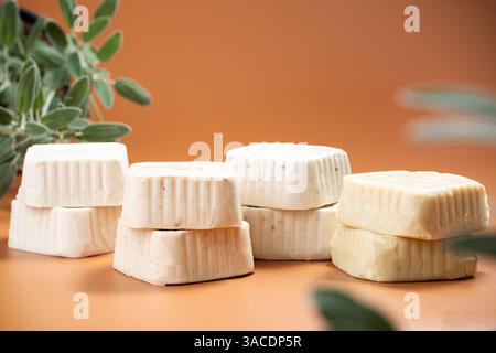 Blocchi di formaggio Vegan assortiti: Vista laterale dei formaggi solidi senza latticini su sfondo arancione con foglie verdi Foto Stock