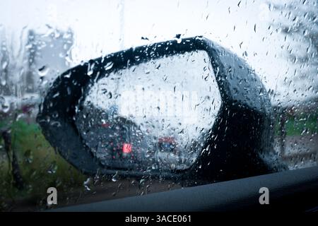 Specchio laterale dell'auto ricoperto da gocce di pioggia con traffico sfocato sullo sfondo Foto Stock